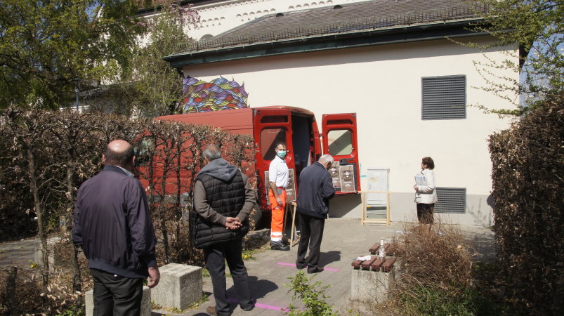 drei Personen warten vor dem Kleintransporter auf die Essensausgabe